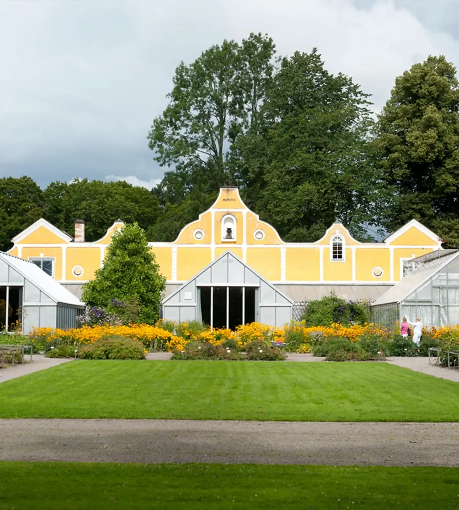 En gul byggnad med tre glasade växthus och planteringar framför.